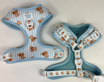 May include: Two dog harnesses with a blue and white striped pattern and a repeating teddy bear design. The harnesses have adjustable straps and white plastic buckles. One harness has the text "RUFF LIFE".