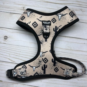 Könnte beinhalten: Ein beigefarbenes Hundegeschirr mit schwarzem Besatz und einem schwarz-weißen Südwest-Druck mit Kaktus- und Schädelmotiven. Das Geschirr trägt den Schriftzug "RUFF LIFE CLOTHING CO.".