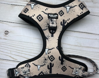 May include: A beige dog harness with black trim and a black and white southwestern print featuring cactus and skull designs. The harness has the text "RUFF LIFE CLOTHING CO." printed on it.