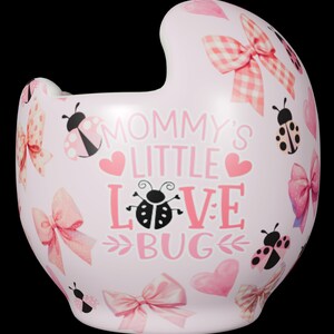 Peut inclure: Un bol en céramique rose clair avec un bord découpé, orné d'un motif répétitif de nœuds, de cœurs et de coccinelles roses. Le texte central indique MOMMY'S LITTLE LOVE BUG, avec une coccinelle remplaçant la lettre O dans le mot LOVE.