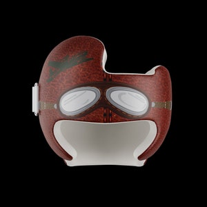 May include: A brown leather baby helmet with a vintage aviator design. The helmet has a pair of goggles and a plane graphic.