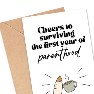 May include: A white card with black text that reads "Cheers to surviving the first year of parenthood". A black and white illustration of a baby bottle and a coffee cup is below the text.