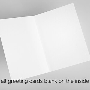 May include: Blank greeting card with a white background. The card is folded in half and is lying flat on a gray surface.