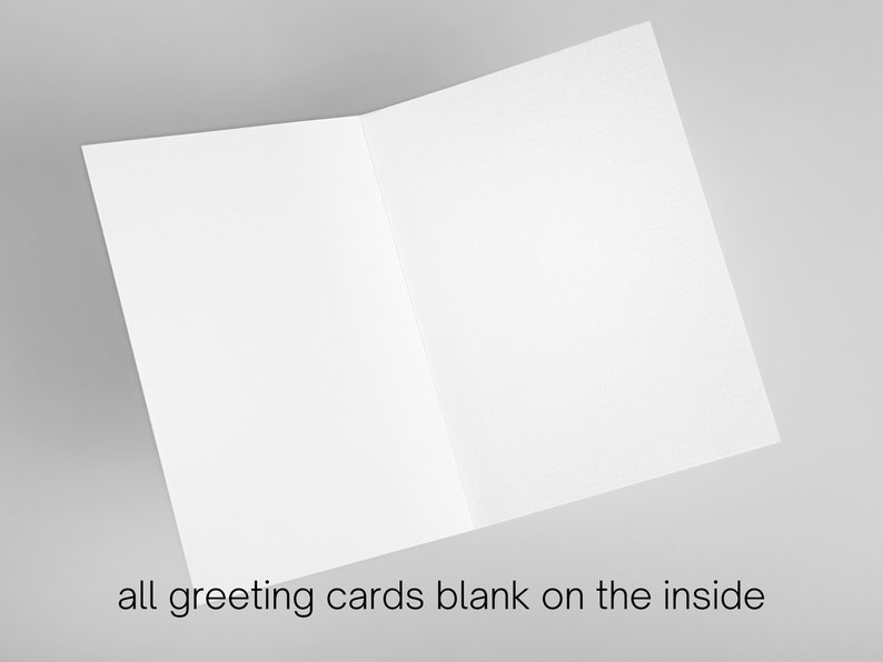 May include: Blank greeting card with a white background. The card is folded in half and is lying flat on a gray surface.