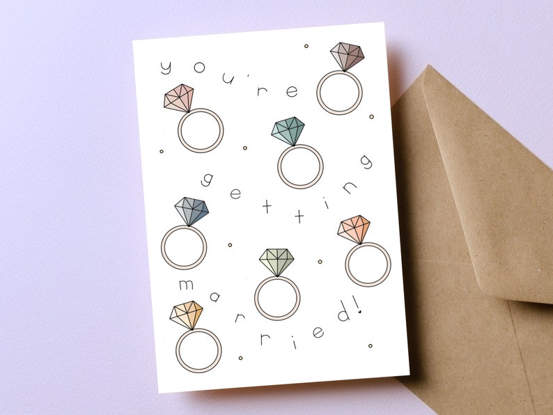 May include: A white card with the text "you're getting married!" surrounded by six rings with different colored diamonds. The rings are outlined in black.