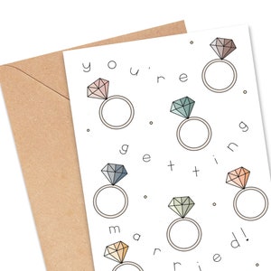 May include: A white card with the text "you're getting married!" in black. The card is decorated with six colorful diamond rings.