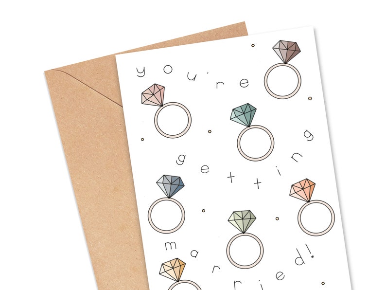 May include: A white card with the text "you're getting married!" in black. The card is decorated with six colorful diamond rings.