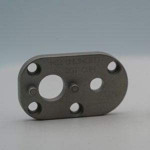 Może przedstawiać: Srebrna metalowa płytka z otworem w środku i kilkoma mniejszymi otworami wokół krawędzi. Na płytce wygrawerowano tekst "REMARKABLE" i "DOT COM". Na zdjęciu znajduje się również srebrna metalowa śruba.