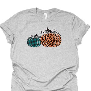 May include: A gray t-shirt with a design of two pumpkins. One pumpkin is teal plaid and the other is orange with a black leopard print.