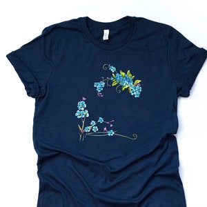 May include: A navy blue t-shirt featuring a floral design of blue and yellow flowers. The flowers are arranged in two clusters on the front of the shirt. The shirt has short sleeves and a crew neck.