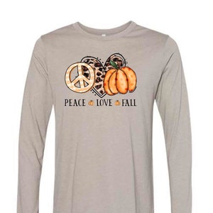 May include: A long-sleeved, light gray t-shirt with a graphic design of a peace sign, a heart with leopard print, and a pumpkin. The text "Peace Love Fall" is printed below the graphic.