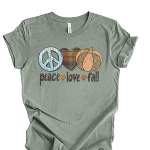 May include: A sage green t-shirt with a peace sign, heart, and pumpkin graphic. The text "peace love fall" is printed below the graphic.
