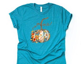 May include: A teal blue t-shirt with a floral pumpkin design. The pumpkin is made of patchwork fabric with a plaid pattern and floral accents.