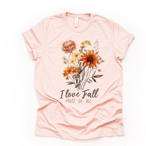 May include: A pink t-shirt with a floral design and the text "I love Fall -most of all- "