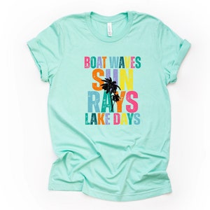 May include: A light blue t-shirt with a colorful graphic design that reads "Boat Waves Sun Rays Lake Days". The graphic features palm trees and a distressed vintage look.