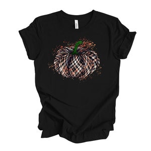 May include: Black t-shirt with a graphic of a plaid pumpkin with a green stem. The pumpkin is surrounded by orange and white splatters.