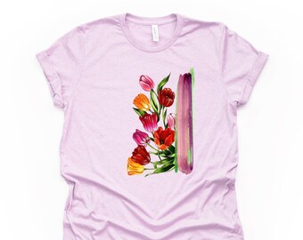 May include: A light purple t-shirt featuring a watercolor design of colorful tulips in shades of red, orange, and pink. A vertical purple and green brushstroke is next to the flowers. The shirt has short sleeves and a crew neck.