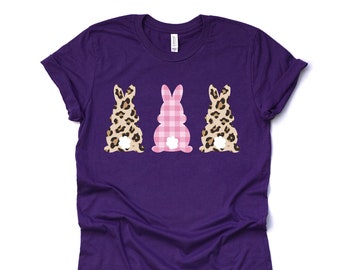 May include: Purple t-shirt with three bunny silhouettes. The center bunny is pink and white gingham. The bunnies on either side are brown and black leopard print.