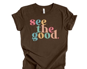 May include: A brown t-shirt with the text "see the good" in colorful letters. The letters are in a retro font style.