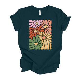 May include: A dark teal t-shirt with a graphic print of five stylized flowers in shades of pink, orange, yellow, and green. The flowers are arranged in a rectangular shape.