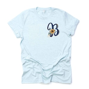 May include: A light blue t-shirt with a navy blue letter "B" with a sunflower graphic on the front.