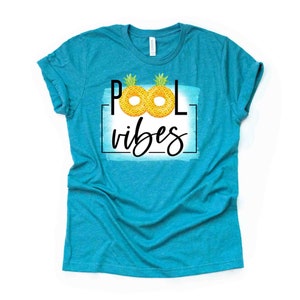 May include: A turquoise blue t-shirt with the text "Pool vibes" in black lettering. Two yellow pineapple pool floats are incorporated into the "O" in the word "Pool".