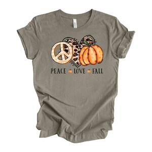 May include: A light brown t-shirt with a peace sign, a leopard print heart, and a pumpkin with the text "Peace Love Fall".
