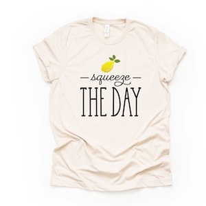 May include: A beige t-shirt with a yellow lemon graphic and the text "squeeze the day" in black.