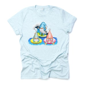 May include: Light blue t-shirt featuring a colorful graphic of three gnomes enjoying summer. One gnome is surfing a wave, while the other two are floating on inflatable rings. The word "Summer" is printed on one of the rings.