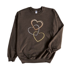 May include: A brown sweatshirt with three interlocking hearts in gold, silver, and rose gold.