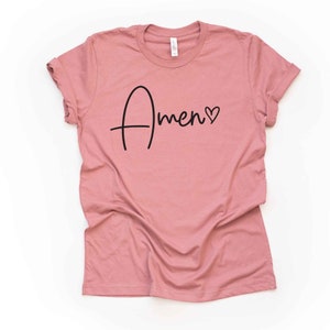 May include: A dusty rose colored t-shirt with a black cursive inscription that reads "Amen" with a small heart symbol.