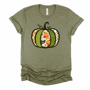 May include: A green t-shirt with a black outline of a pumpkin. The pumpkin is decorated with different patterns, including plaid, polka dots, and floral designs. The pumpkin is filled with orange and green colors.
