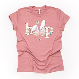 May include: A pink t-shirt with a graphic of a bunny with a floral crown and the word "hop" printed on it.