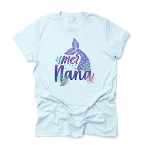 May include: Light blue t-shirt with a mermaid tail and the text "mer nana" in purple and blue lettering. The design includes a mermaid tail, seashells, and seaweed.