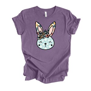 May include: Purple t-shirt with a floral bunny graphic. The bunny has a floral crown and a blue and white patterned face.