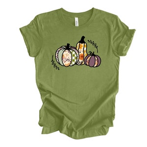 May include: A green t-shirt with a graphic of three pumpkins. The pumpkins are decorated with floral and plaid patterns.