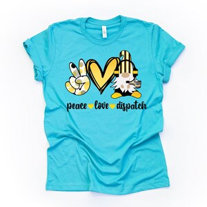 May include: A turquoise blue t-shirt with a peace sign, heart, and gnome graphic. The text "peace love dispatch" is printed below the graphic.