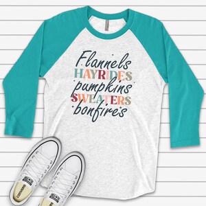 May include: A white and turquoise baseball tee shirt with the text "Flannels, Hayrides, Pumpkins, Sweaters, Bonfires" printed in colorful letters.