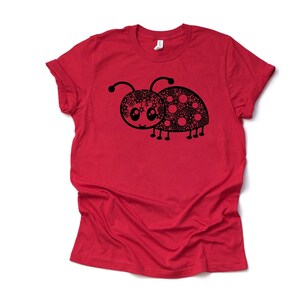 May include: Red t-shirt with a black and white graphic of a ladybug with a floral pattern.