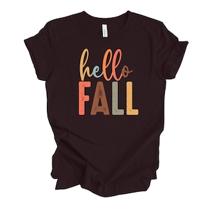 May include: A dark brown t-shirt with the text "hello fall" in colorful, stylized lettering.