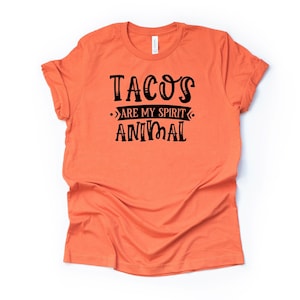 Puede incluir: Camiseta naranja con texto negro que dice "Tacos are my spirit animal".