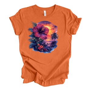 May include: Orange t-shirt featuring a vibrant tropical design. The graphic includes a large purple hibiscus flower, palm trees, and a sunset scene. The design is set within a circular frame, creating a cohesive and eye-catching image.