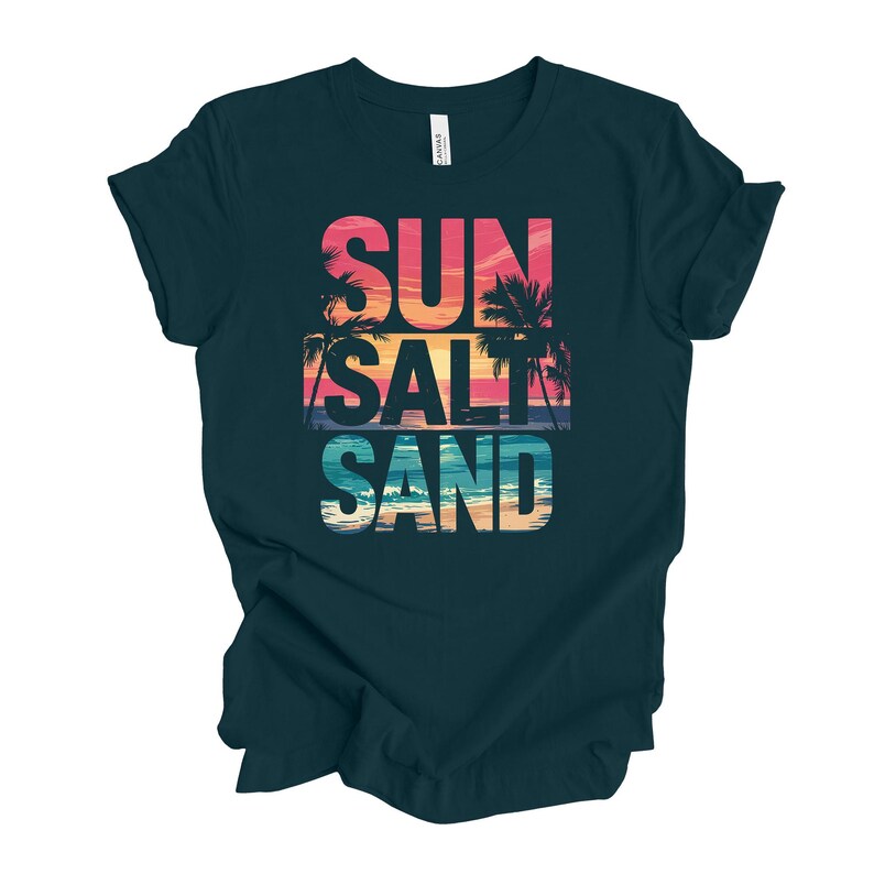 Op de afbeelding: Donker teal t-shirt met de woorden "SUN SALT SAND" in een kleurrijk, gelaagd ontwerp. De tekst bevat een zonsondergang en een palmboomafbeelding. Het shirt is gemaakt van een zacht materiaal.