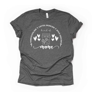 Puede incluir: Una camiseta gris oscuro con un dise&ntilde;o gr&aacute;fico blanco. El dise&ntilde;o presenta una casa con corazones, flores y el texto "Homeschooling + Coffee Drinking + Jesus Seeking + kind of mama".