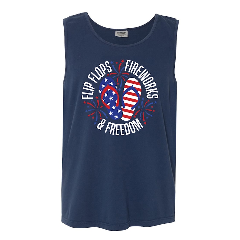 May include: A navy blue sleeveless shirt with a white circle graphic featuring red, white, and blue flip flops and fireworks. The text "Flip Flops & Fireworks & Freedom" is written around the graphic.