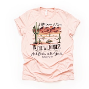 May include: A pink t-shirt with a desert landscape graphic and the text "I Will Make A Way In The Wilderness And Rivers In The Desert Isaiah 43:19".