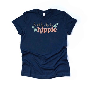 Peut inclure: Un t-shirt bleu marine avec le texte "little bit hippie" en lettres roses et dor&eacute;es avec de petites fleurs vertes et bleues.