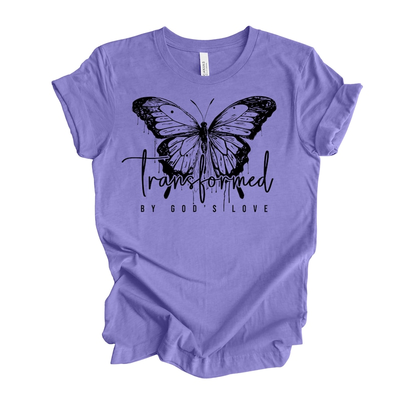 Peut inclure: T-shirt violet avec un motif de papillon noir et le texte "transform&eacute; par l'amour de Dieu".