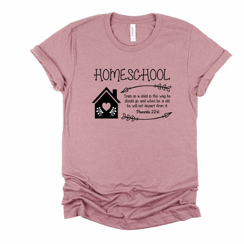 Puede incluir: Una camiseta rosa con el texto "HOMESCHOOL" y una ilustraci&oacute;n negra de una casa con un coraz&oacute;n y flores. El texto "Train up a child in the way he should go and when he is old, he will not depart from it. Proverbs 22:6" tambi&eacute;n est&aacute; impreso en la camiseta.
