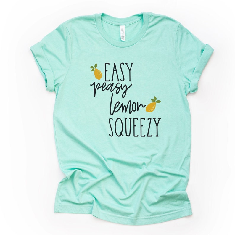 Puede incluir: Una camiseta azul claro con el texto "Easy peasy lemon squeezy" en letras negras y dos limones amarillos con tallos verdes.